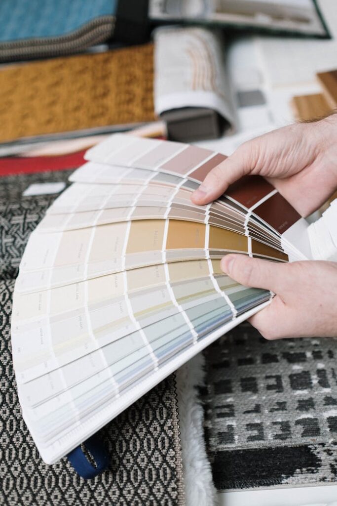 L'importanza delle pitture in una ristrutturazione edile Hands holding a fan of color swatches against a backdrop of fabric samples, ideal for interior design projects.