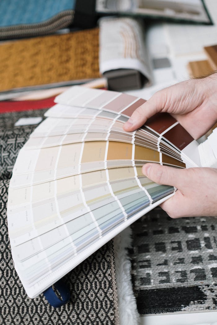 L'importanza delle pitture in una ristrutturazione edile Hands holding a fan of color swatches against a backdrop of fabric samples, ideal for interior design projects.